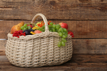 Wicker basket with different fresh fruits on wooden background