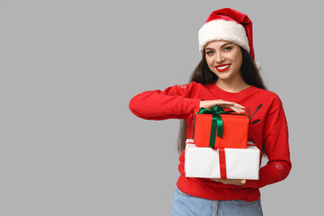 Beautiful young woman in Christmas sweater with gift boxes on grey background