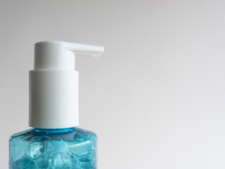 Close-up of a blue gel dispenser bottle with a white cap and a drop of soap on the nozzle. The bottle contains bubbling gel. It rests against a neutral gray background that provides ample copy space