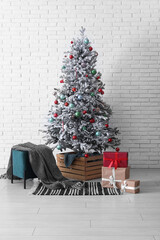 Decorated Christmas tree with gifts and pouf against white brick wall