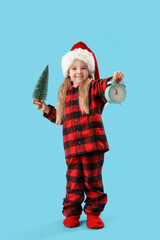 Obraz premium Cute little girl with alarm clock and small Christmas tree on blue background