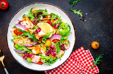 Foodie food salad with baked salmon and tomatoes, cucumber, arugula, radicchio, onion and lettuce with lemon and olive oil dressing.  Brown background, top view