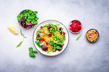 Vegan salad with baked beets, tangerine, red onion, lettuce, sesame and arugula, gray background, top view