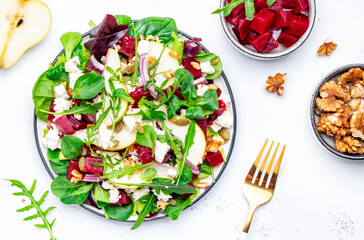 Foodie food salad with baked beet and ricotta cheese, pear, pumpkin seeds, arugula, lettuce, onion and walnuts on white background, top view