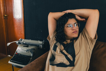 Mujer latina sentada en un sillon a un lado de una maquina de escribir retro