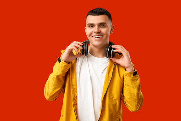 Young man in stylish jacket and headphones on red background
