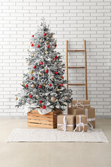Beautiful Christmas tree, gift boxes and ladder near light brick wall