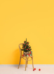 Wooden chair with Christmas tree in pot and gifts near orange wall