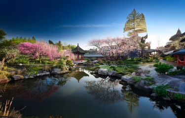 Fototapeta premium A tranquil Asian-style garden with a pond reflecting the lush greenery and a wooden pagoda.