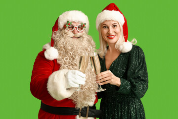 Santa Claus and beautiful mature woman in Christmas hats with glasses of champagne on green background