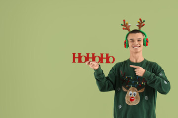 Teenage boy in reindeer horns pointing at Christmas greeting on green background
