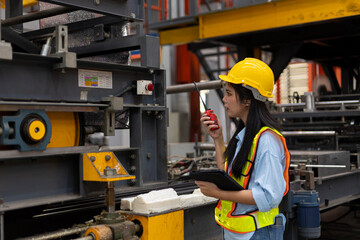 Female attractive engineer or technician using computer tablet to monitor the function of a machinery system in a steel factory. Female mechanical engineer in a safety wear checking a heavy machine