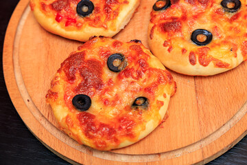 Three small pizzas with olives on top sit on a wooden cutting board