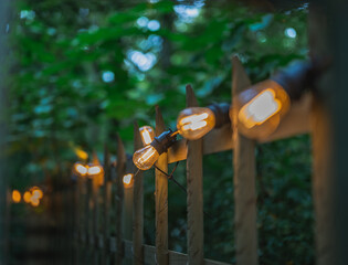 Chain of light bulbs on wooden fence in the city park