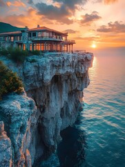 A large house perched precariously on a cliff overlooking the ocean at sunset.