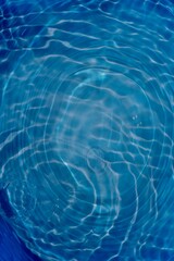 Blue water with ripples on the surface. Defocus blurred transparent blue colored clear calm water surface texture with splashes and bubbles. Water waves with shining pattern texture background.