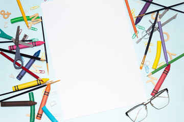 Desk with art tools, stationery and other school supplies around a blank sheet of paper on a blue background...Space for creativity