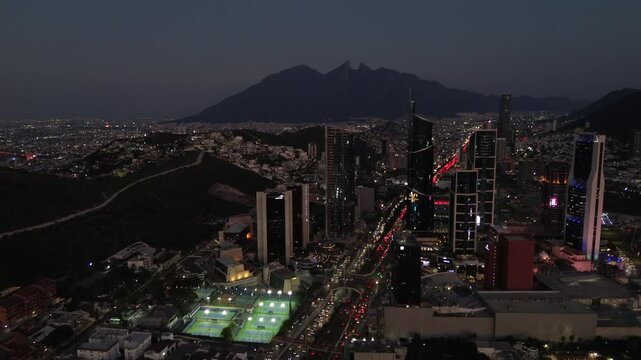 Ciudad grande con edificios muy altos en elnorte de mexico y de fondo un cerro emblamatico de la ciudad, cerro de la silla la ciudad mas avanzada de mexico con trafico moderado al caer el atardecer 