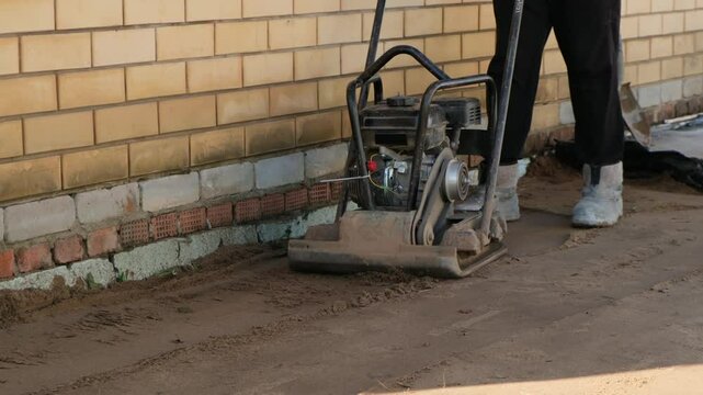Worker using vibrating soil compactor for sand ramming. Construction and renovation.