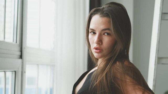 Portrait of young beautiful model posing in black lingerie and stockings near a large window. Calm cute brunette in fashionable lingerie.