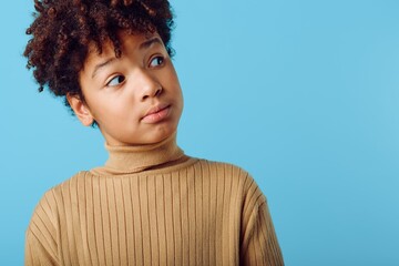 Curious young african american girl in turtleneck sweater looking upward with wonder and...