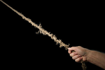 A man's hand pulls an old rope going into infinity. Concept of time. Isolate on black.