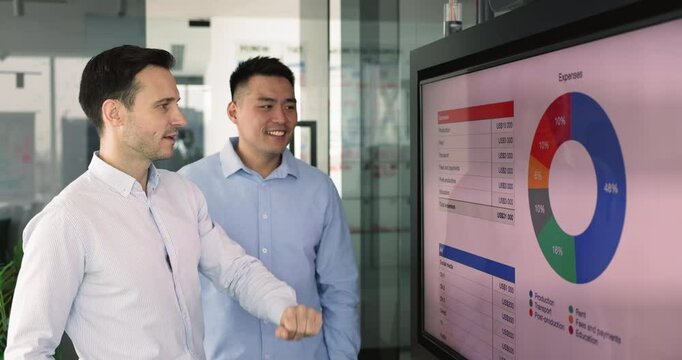Two multiethnic men colleagues review charts with infographic data, analyzing allocation of expenses across different categories to assess efficiency and effectiveness of business financial management - Powered by Adobe