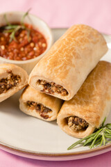Sausage rolls stacked against a pink background