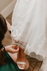 Bridesmaid fastening the bride’s pearl-embellished shoe