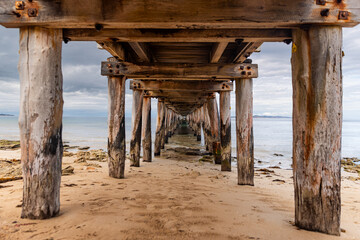 View under Point Lonsdale Pier with weathered wooden pillars on beach