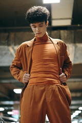 Fashionable young man in a brown outfit poses confidently in an urban indoor setting