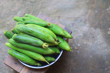 A bowl of fresh green ridge gourds (sponge gourds) placed on a wooden surface with a rustic background