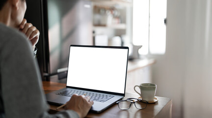 A close-up image of a man working on laptop computer at a table at home, typing on the laptop...