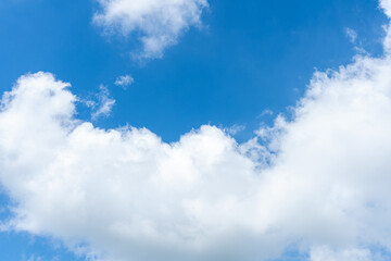 Fluffy white clouds drift across a clear blue sky, casting soft shadows on the landscape below