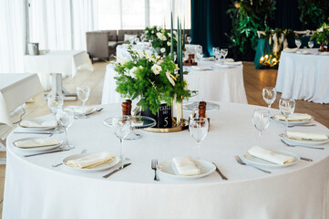 Luxurious restaurant. Luxurious interior, white tables, serving dishes and glasses for guests. Green decor