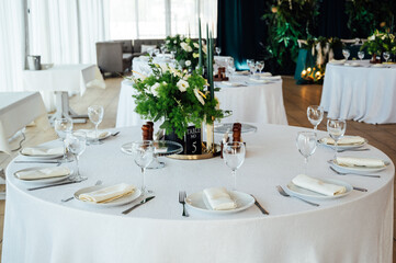 Luxurious restaurant. Luxurious interior, white tables, serving dishes and glasses for guests. Green decor