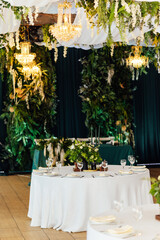 Luxurious restaurant. Luxurious interior, white tables, serving dishes and glasses for newlyweds. Green decor