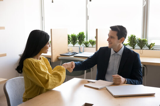 Happy diverse couple of business professional partners shaking hands at meeting table after conversation, corporate discussion, job interview, getting successful agreement, partnership