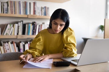 Serious young Indian accountant girl analyzing contract, financial terms, checking investment...