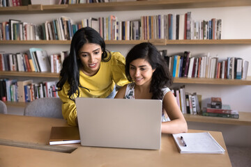 Positive young adult Indian students working on research study, educational project at laptop...