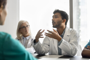 Inspired young male doc gp therapist speak to coworkers at work briefing at boardroom share...