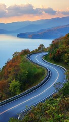 Obraz premium A curved road winds through the heart of a mountain range, leading the eye to a tranquil lake nestled in the distance Mountains rise majestically in the backdrop