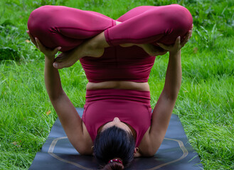 Young brown-haired woman performing an inverted yoga pose on her mat outdoors in nature wearing a...