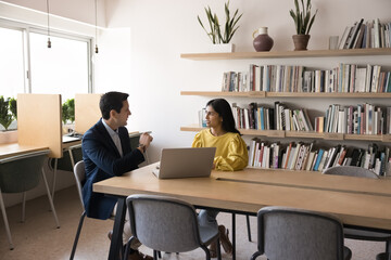 Serious multiethnic boss and manager discussing project strategy, teamwork in office co-working room, meeting at large table, talking. Male tutor training student girl in library
