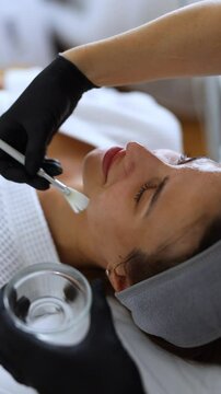 Cosmetologist performs a facial peeling procedure on a young woman.