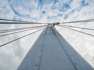 Fototapeta premium A bridge with a long white pillar and a cloudy sky in the background. The bridge is tall and the sky is overcast. Design and engineering. Modern bridge with suspension metal cords.