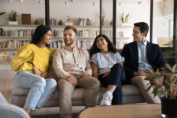 Fototapeta premium Multiethnic team of cheerful young adult students enjoying work break on couch in professional training center, talking, chatting, smiling, laughing. Casual portrait of diverse office friends