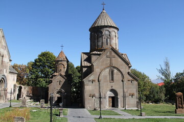 Fototapeta premium The ancient church stands in a lush green field. Its rough-hewn stone walls and simple cross roof are surrounded by trees and thick, vibrant grass, showcasing its historical significance.