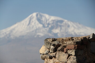 This breathtaking view features a snow-capped mountain peak towering over ancient stone wall ruins, illustrating the beauty of nature alongside the remnants of history in a serene landscape.