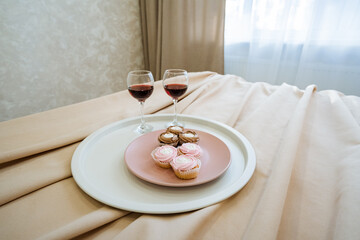A delightful plate filled with an assortment of cupcakes and two elegant glasses of wine sitting gracefully on a neatly made bed, creating an inviting and cozy atmosphere